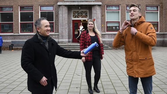 Remco Neumann (Havenbedrijf Rotterdam) deelt onder toeziend oog van hoofd van de school Louisette Bronsgeest 90 hervulbare flesjes uit aan leraar Geert-Jan van der Spek van basisschool De Klaver op Rotterdam, Heijplaat (foto Ries van Wendel de Joode)