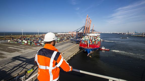 Man op containerkraan uitzicht haven en containerschip aan terminal