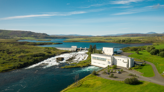 Wasserkraftwerk in Island in grüner Umgebung mit Wasserfall und blauem Himmel
