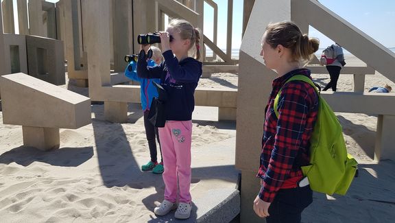 A girl looks at the ships with binoculars