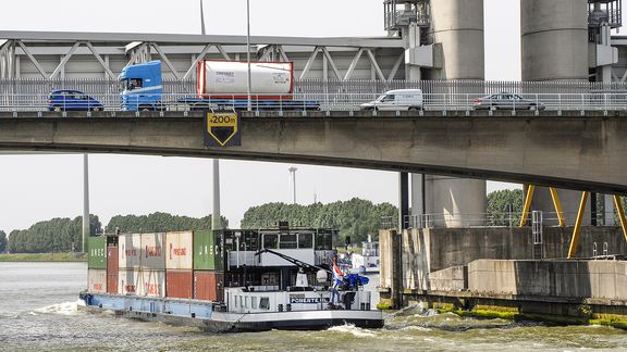 Brug met auto's en vrachtwagen, eronderdoor vaart een binnenvaartschip met containers