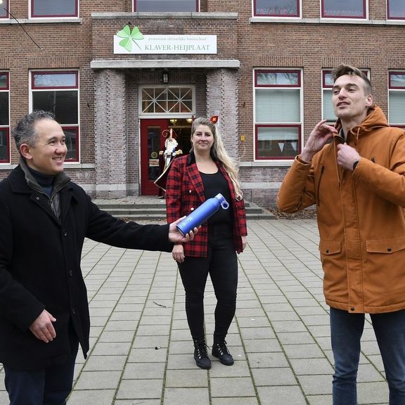   Remco Neumann (Hafenbetrieb Rotterdam) verteilt unter Aufsicht der Schulleiterin Louisette Bronsgeest 90 Mehrwegfläschchen an den Lehrer Geert-Jan van der Spek der Grundschule De Klaver in Rotterdam, Heijplaat