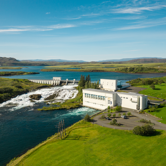 Waterkrachtcentrale in IJsland in een groene omgeving met waterval en blauwe lucht