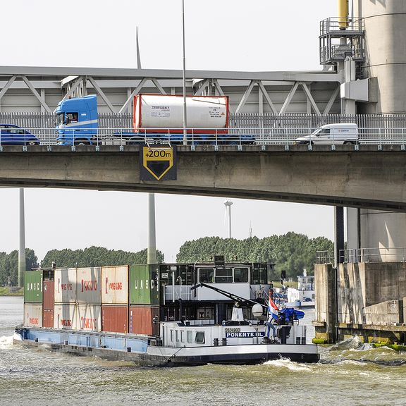 Brug met auto's en vrachtwagen, eronderdoor vaart een binnenvaartschip met containers