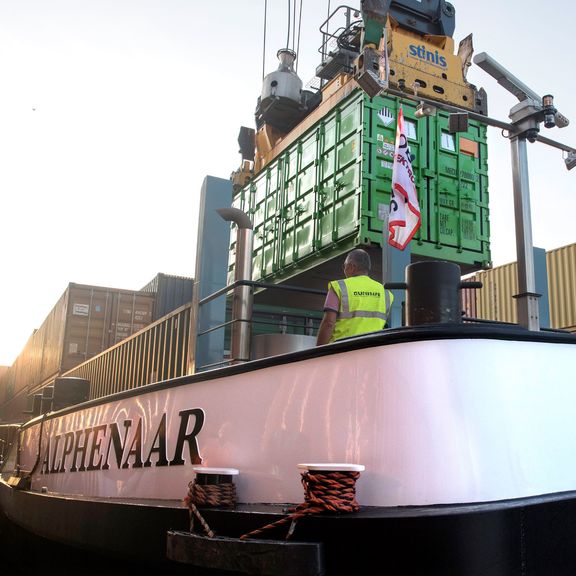 Die ersten beiden Containerbatterien werden auf das Binnenschiff Alphenaar verladen