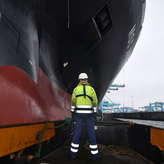 Oarsman waits on mooring line near container ship