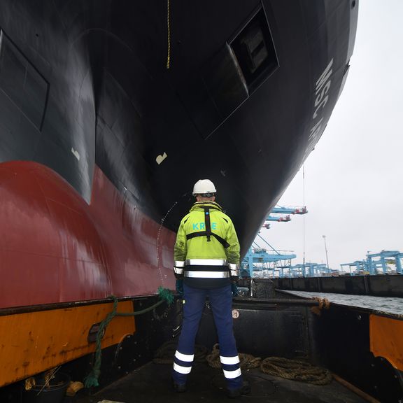 Roeier wacht op tros bij containerschip